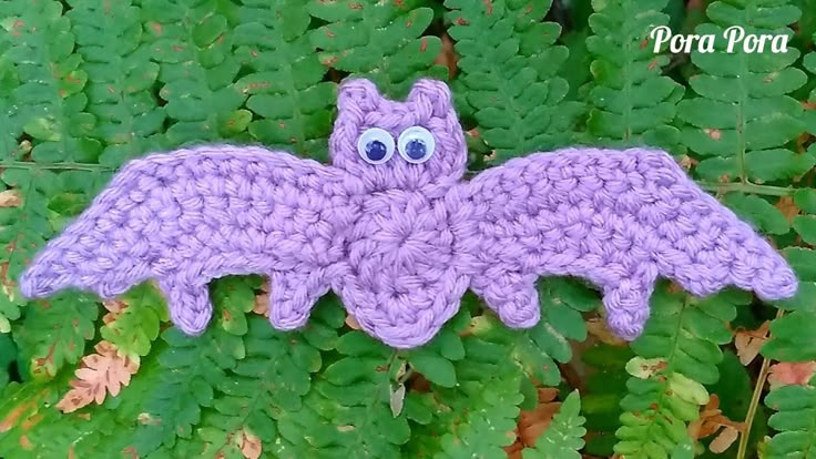 a purple crocheted bat sitting on top of some green plants with eyes drawn on it