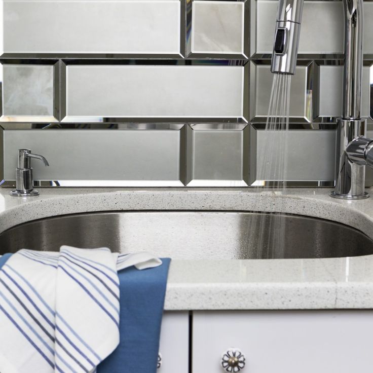 a stainless steel sink and faucet in a kitchen with glass tiles on the wall