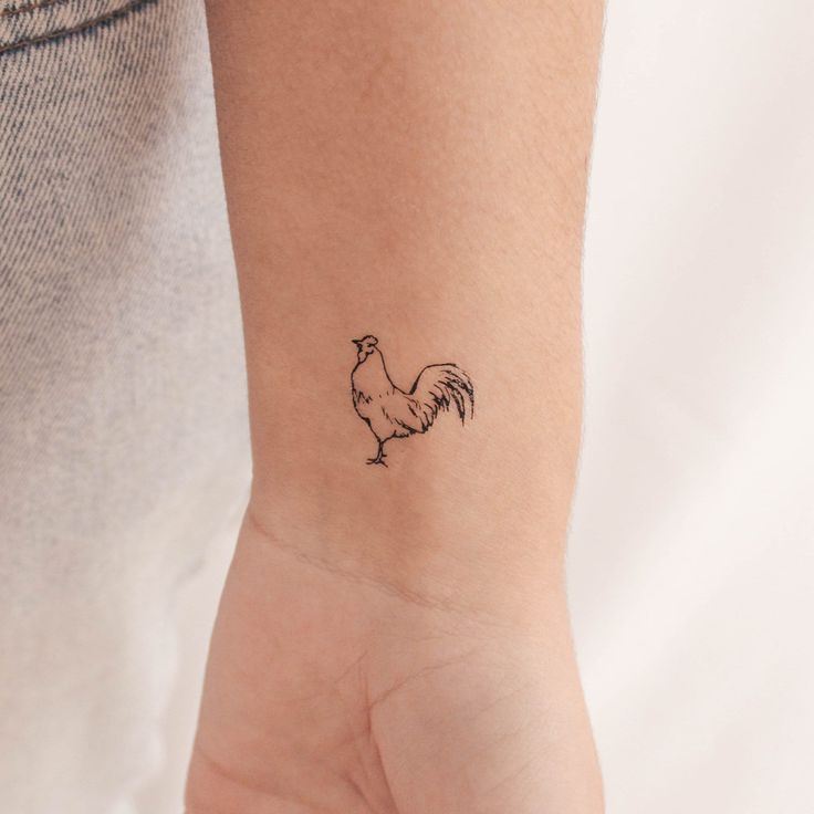 a small tattoo on the wrist of a woman with a rooster drawn on her arm