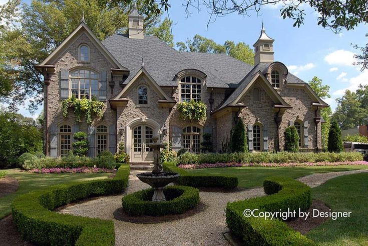 a large stone house surrounded by lush green grass and flowers with a fountain in the front yard