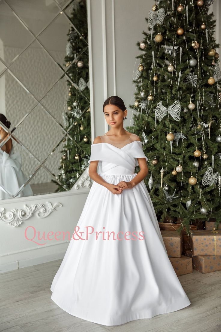 a woman standing in front of a christmas tree wearing a white dress with ruffles