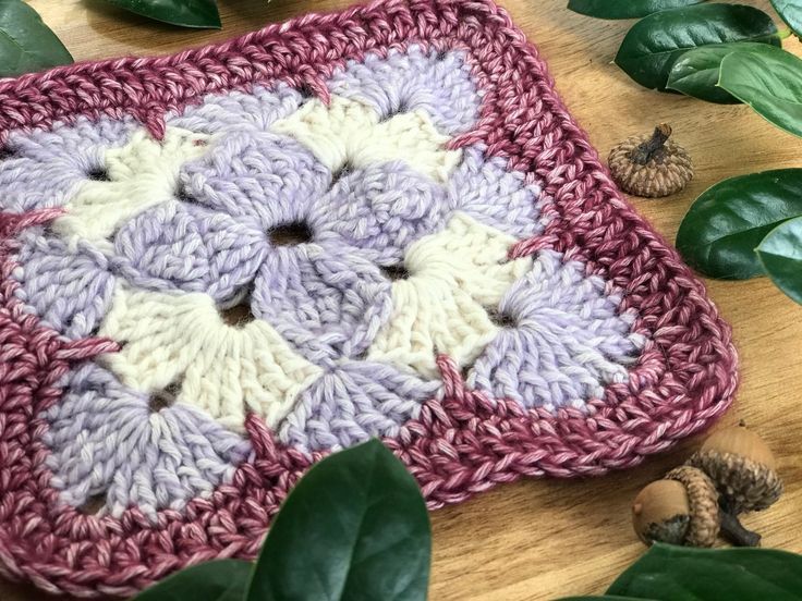 a crocheted square with white and purple flowers on it next to some leaves