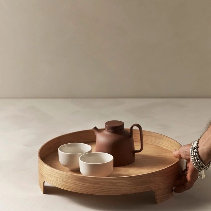 a person holding a tray with two cups and a teapot on it