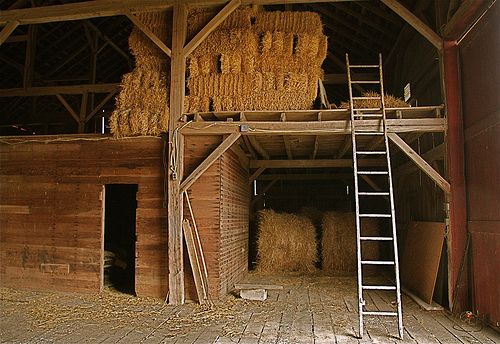 an old barn with hay bales in the doorway and ladders leading up to it