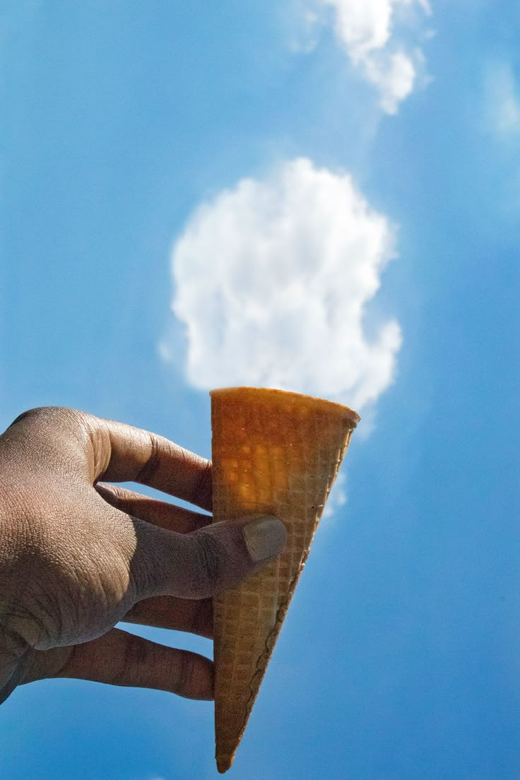 a hand holding an ice cream cone under a blue sky