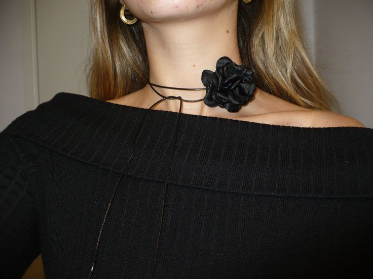 a close up of a woman wearing a black sweater with a flower on the collar