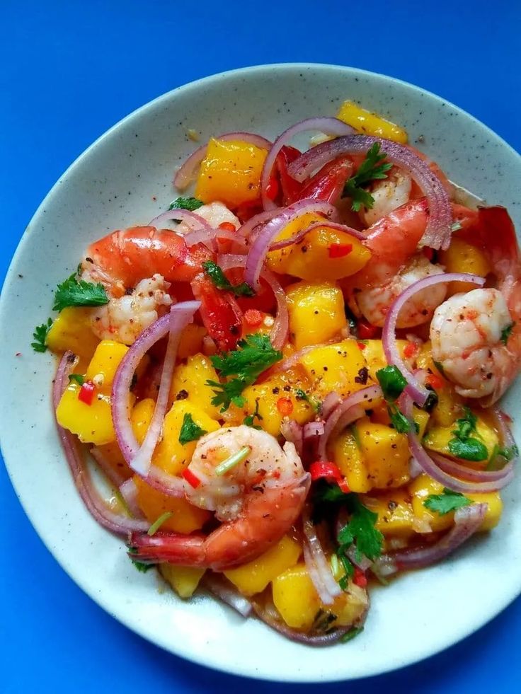 a white plate topped with shrimp and pineapple salad on top of a blue table