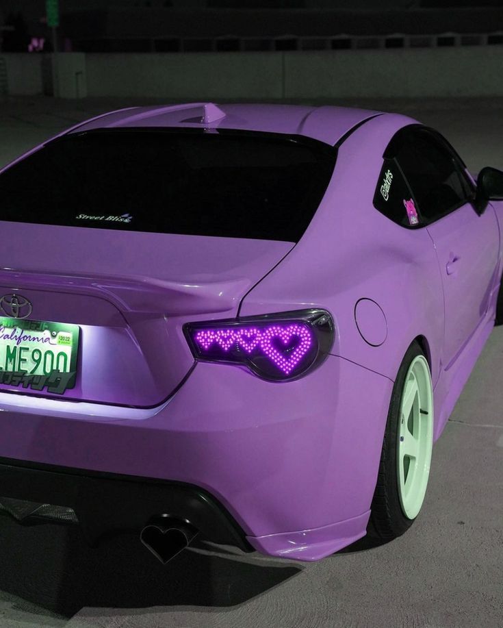 a purple car parked in a parking lot at night with its license plate on it