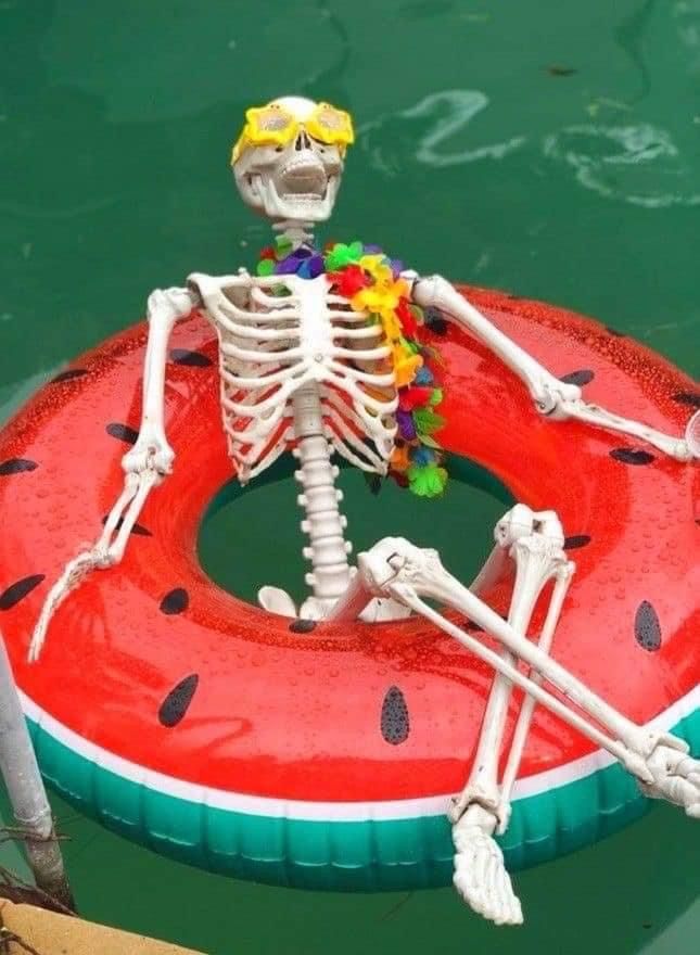 a skeleton sitting on top of an inflatable watermelon raft floating down a body of water