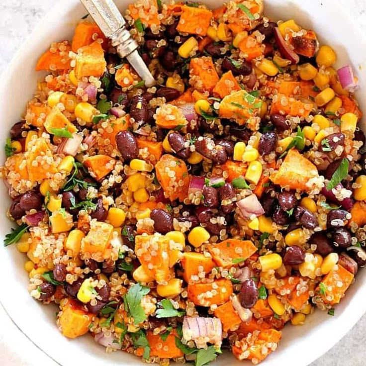 a white bowl filled with black beans, corn and quinoa salad on top of a checkered table cloth