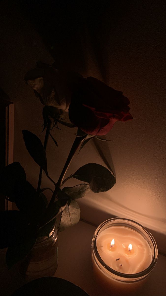 a lit candle next to a rose in a vase