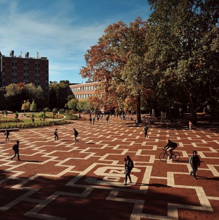 many people are walking and riding bikes in a park with red brick tiles on the ground