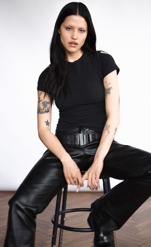 a woman sitting on top of a stool wearing black leather pants and boots with tattoos