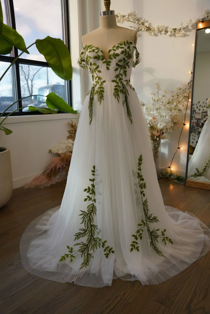 a wedding dress on display in front of a window with lights and greenery around it