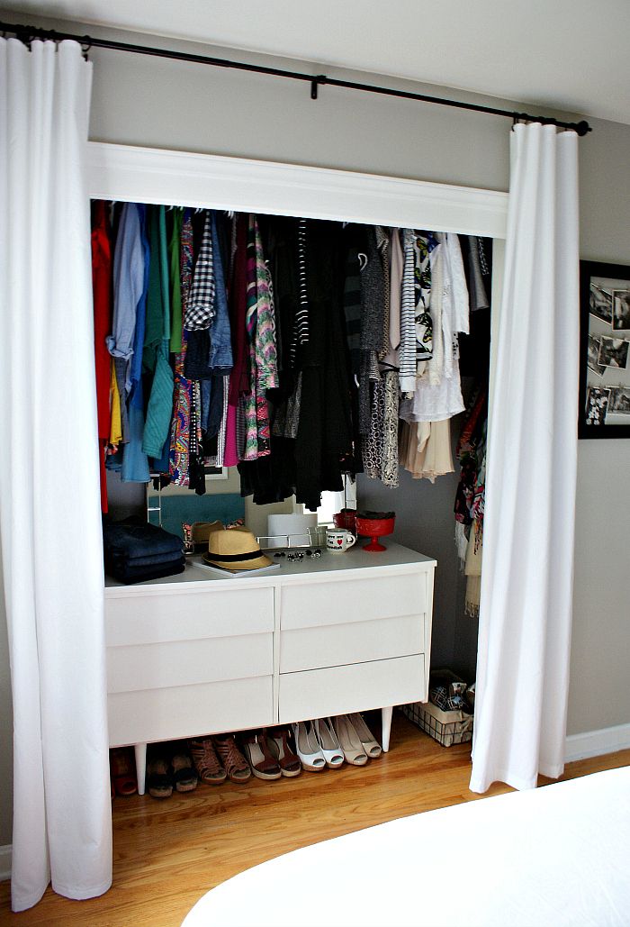 a closet with clothes and shoes hanging on the wall, next to a white bed