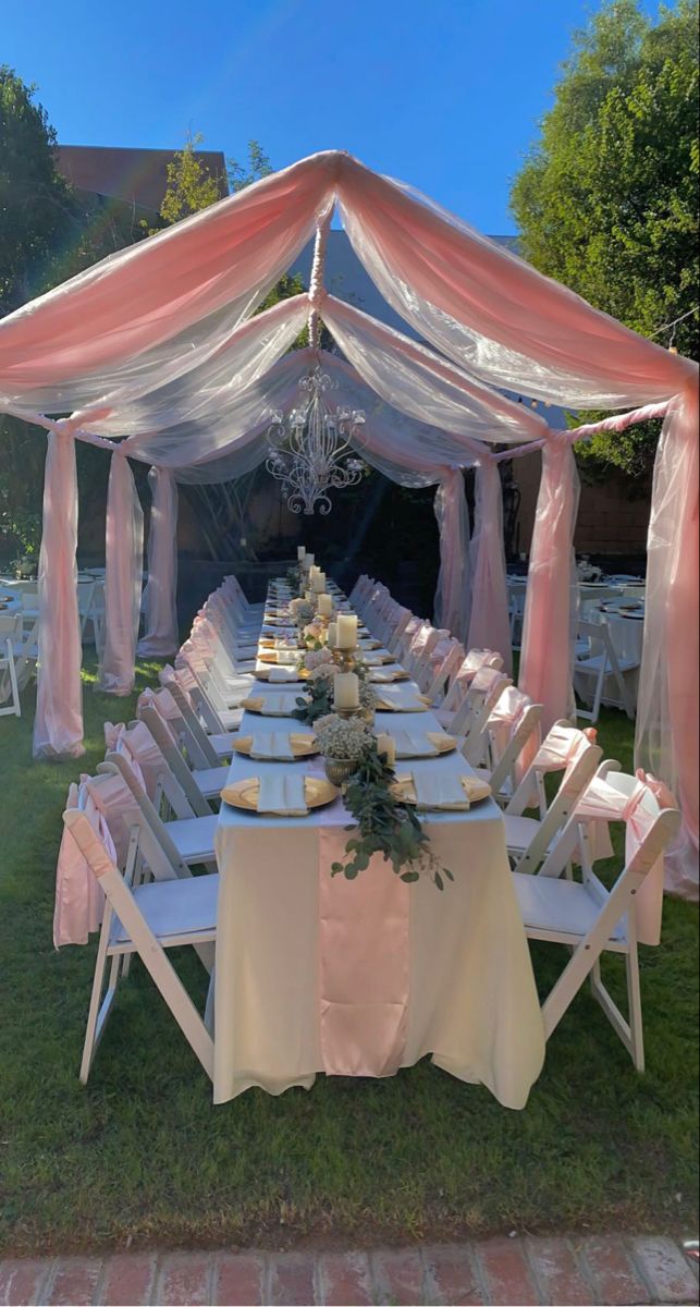 a table set up for a wedding with pink and white draping on it