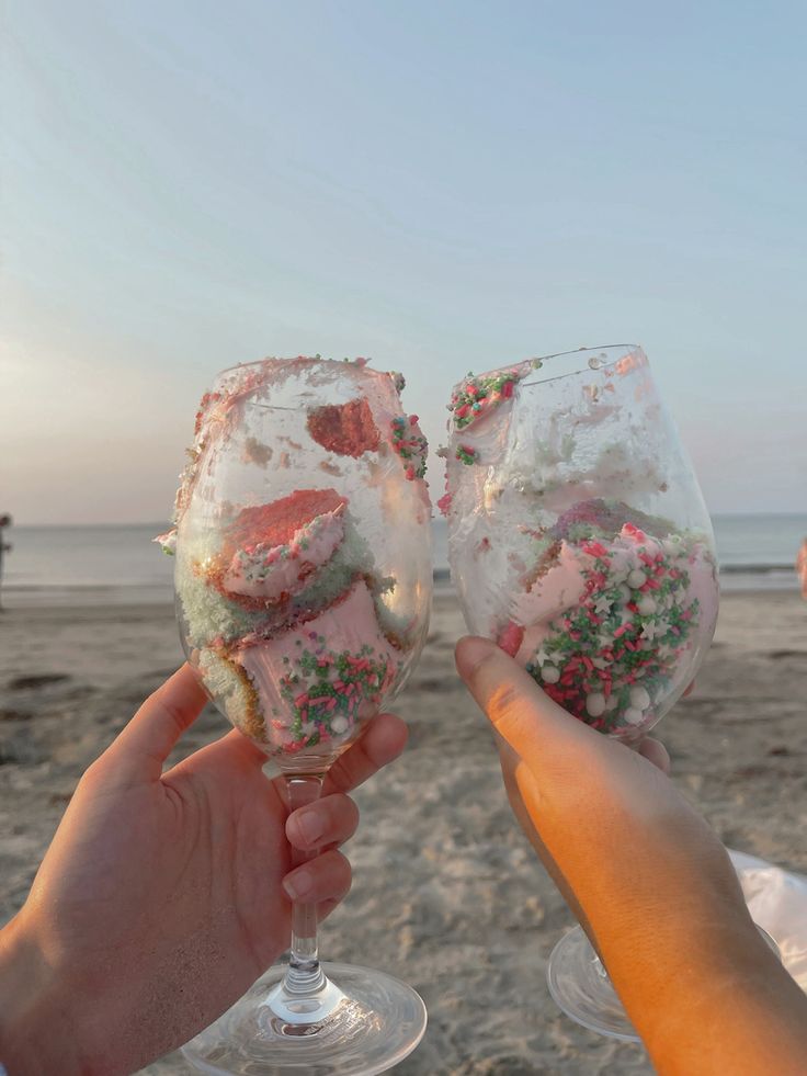 two people toasting wine glasses with sprinkles and seaweed on the beach