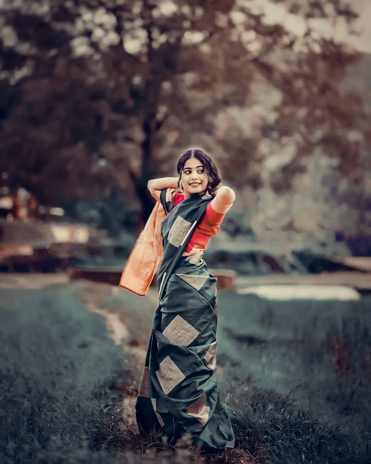 a woman standing in the grass with her arms behind her head, wearing an orange and black sari