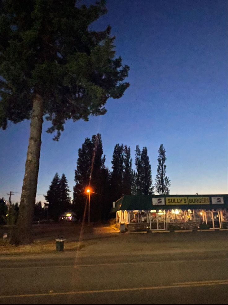 an empty parking lot at night with the lights on and trees in the foreground