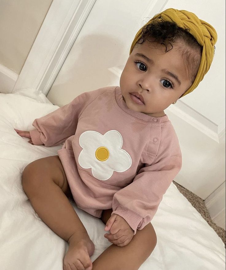 a baby sitting on top of a bed wearing a yellow headband and pink shirt