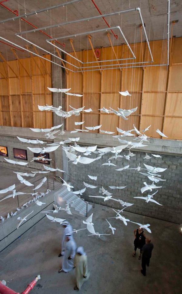 birds are flying in the air above people walking around an indoor area with wood paneling