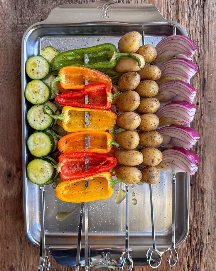 several different types of vegetables in a metal tray on a wooden table with utensils