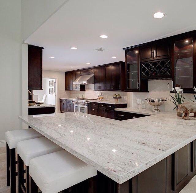 a large kitchen with marble counter tops and dark wood cabinets, along with white stools