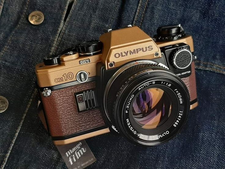 an old camera sitting on top of a pair of blue jeans with the lens attached to it