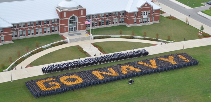 a group of people standing in front of a sign that says go navy on it