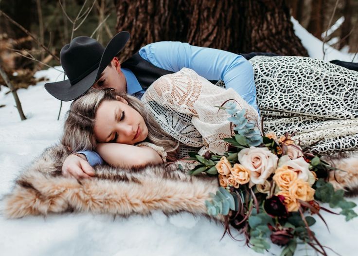 a man and woman laying in the snow next to each other with hats on their heads