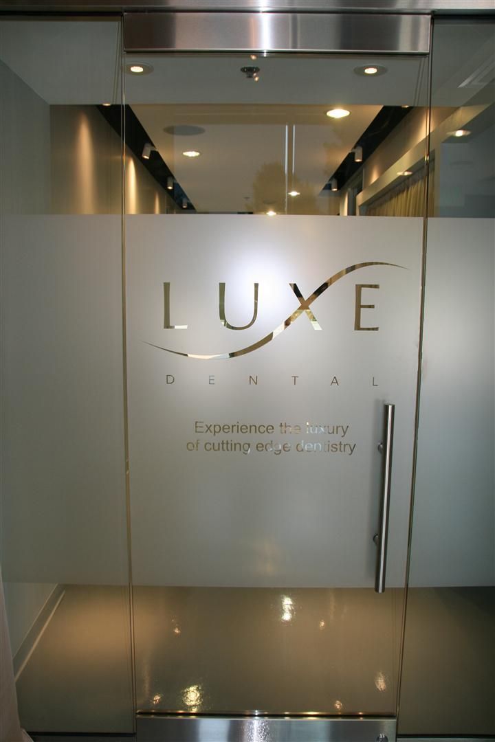 a glass door with the name luxe dental on it in front of a white wall