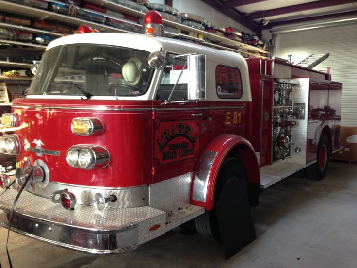 a red fire truck parked in a garage next to a shelf filled with tools and supplies