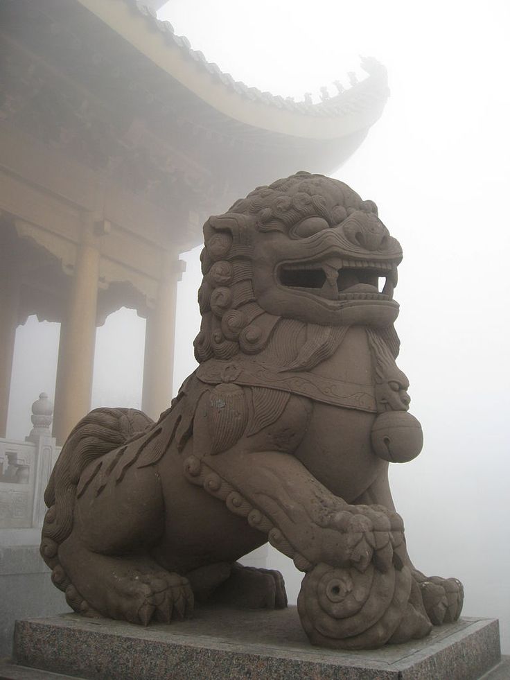 a stone lion statue sitting in front of a chinese building on a foggy day