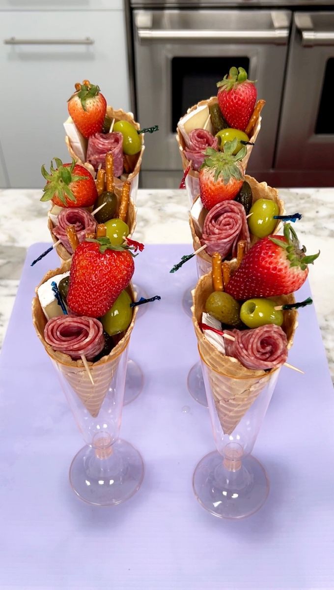 two ice cream cones with strawberries, olives and other fruit in them on a table