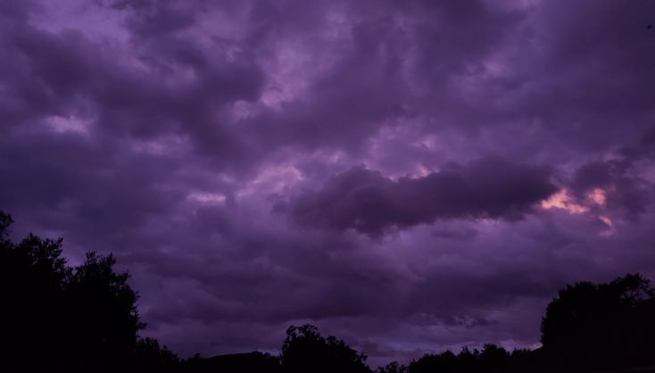 the sky is filled with purple clouds and trees