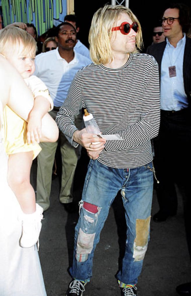 a man in ripped jeans and sunglasses holding a small child while others look at him