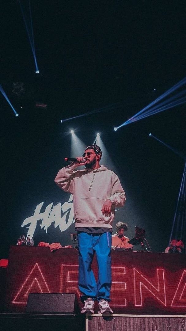 a man standing on top of a stage while wearing a pink sweatshirt and blue jeans