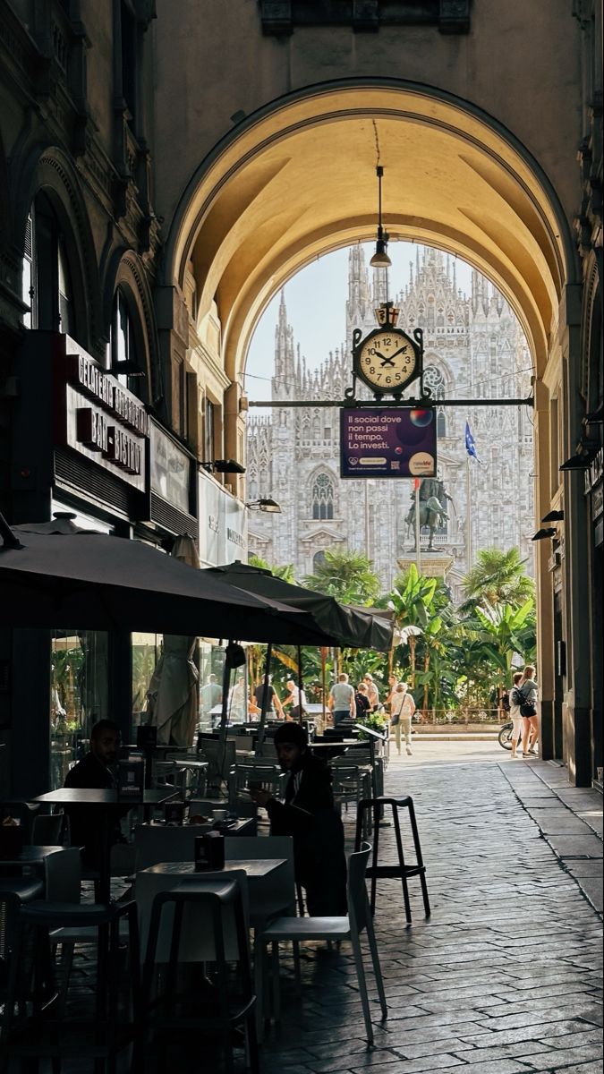 an archway leading into a building with tables and umbrellas