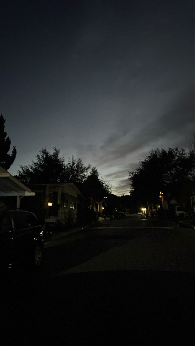 a dark street at night with the moon in the sky and some houses on the other side