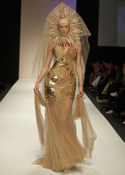 a woman walking down a runway wearing a gold dress