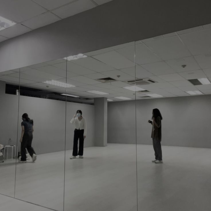 three people standing in an empty room with mirrors