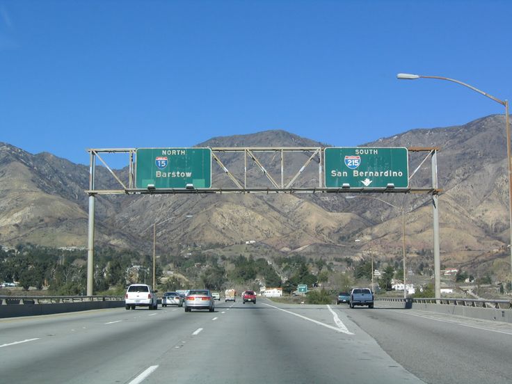 cars driving on an interstate with mountains in the background and blue skies above them as well