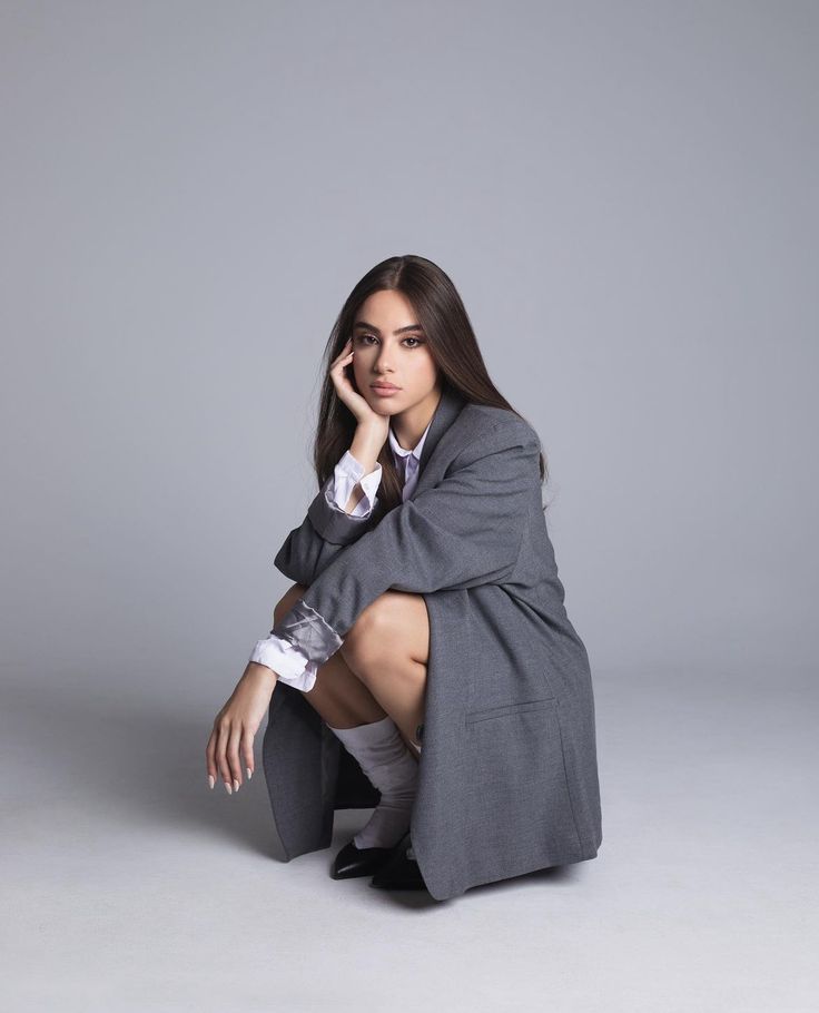 a woman sitting on the ground with her legs crossed and wearing a coat over her shoulders