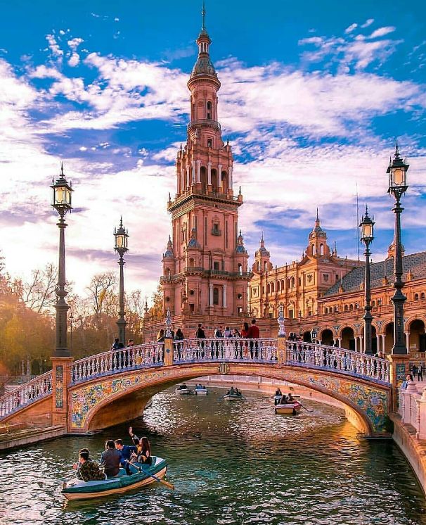 people are riding on boats in the water near a bridge with a clock tower behind them