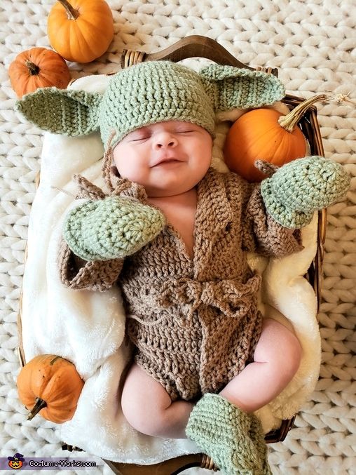 a baby wearing a knitted yoda outfit laying on top of a blanket next to pumpkins