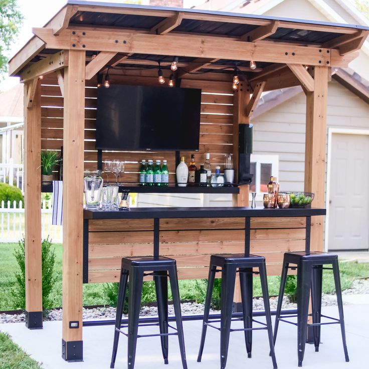 an outdoor bar with stools and television mounted to the wall, in front of a house