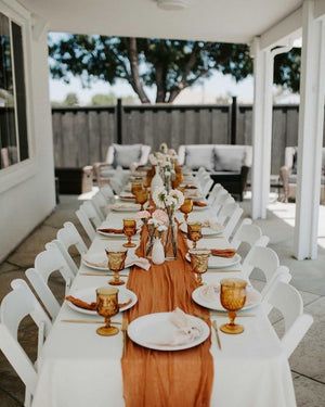 an outdoor dining area with white chairs and orange table cloths on the long tables