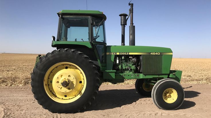 a green tractor parked on top of a dirt field next to a large yellow wheel