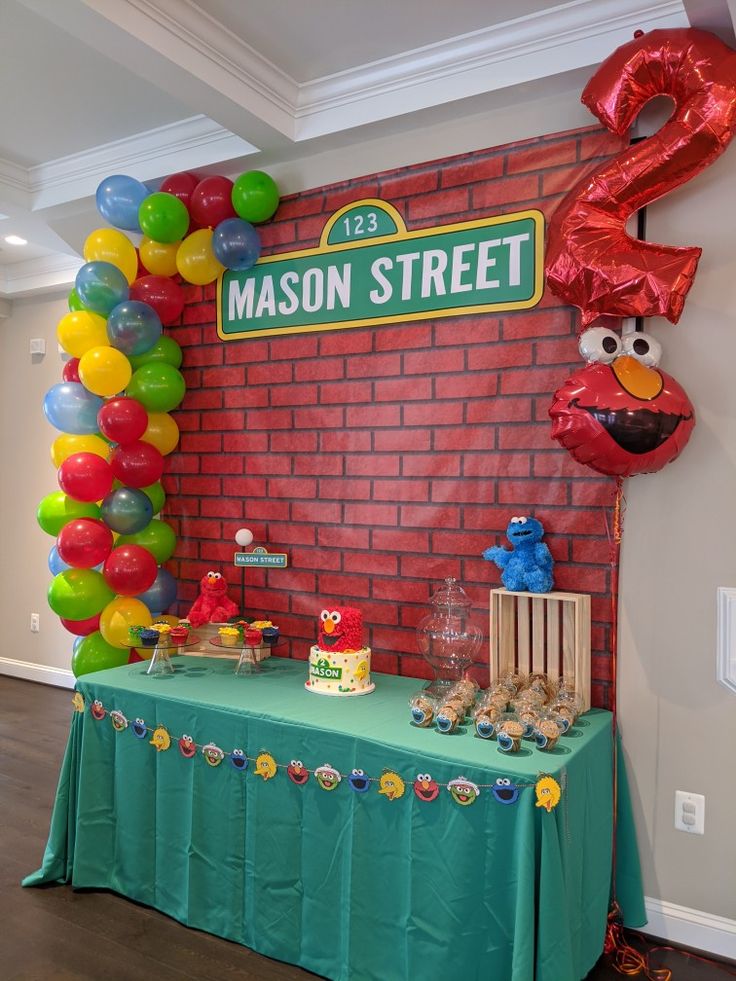 a sesame street birthday party complete with balloons and cake on a table in front of a red brick wall