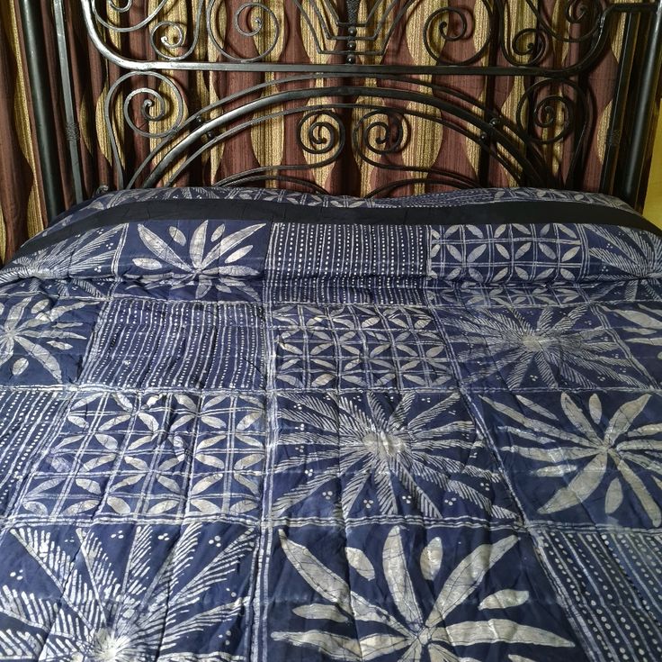 a bed with a blue quilt on top of it next to a metal headboard